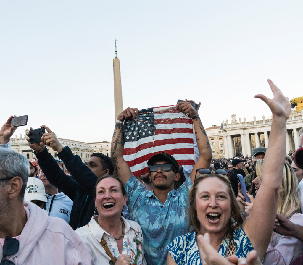 Americans, including one holding an American flag, cheer in St. Peter’s Square.